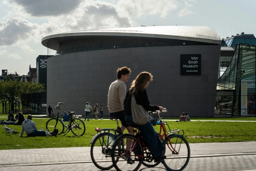 Two cyclists ride in front of the Van Gogh Museum.