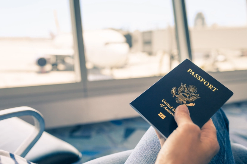 Man holding a passport in an airport waiting area.
