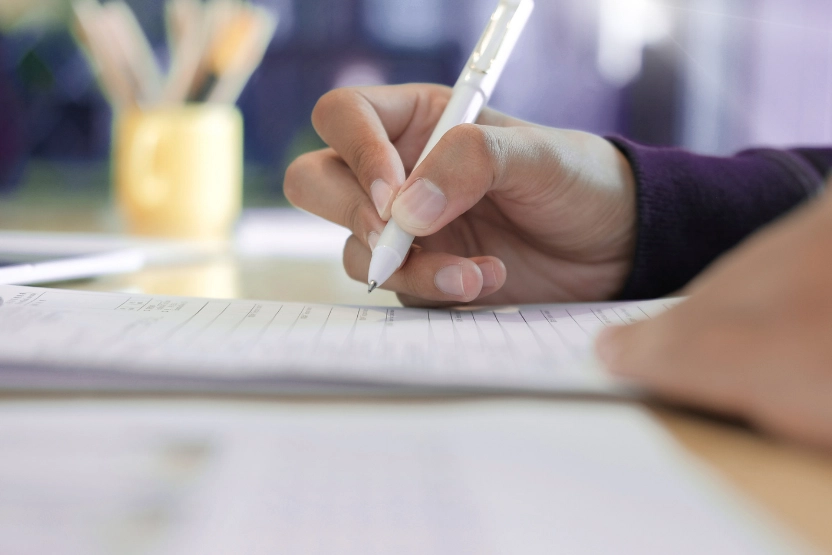 Close up of a hand filling out a form with a white pen